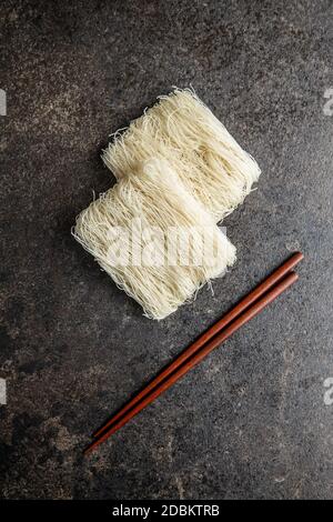 Uncooked white rice noodles and chopsticks on black table. Top view. Stock Photo