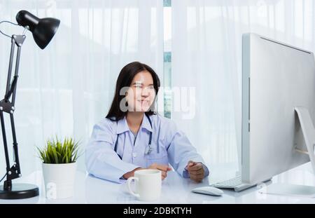 Asian young beautiful woman doctor video call conference online sit listen  patient to explain on front desktop PC computer monitor quarantines diseas Stock Photo