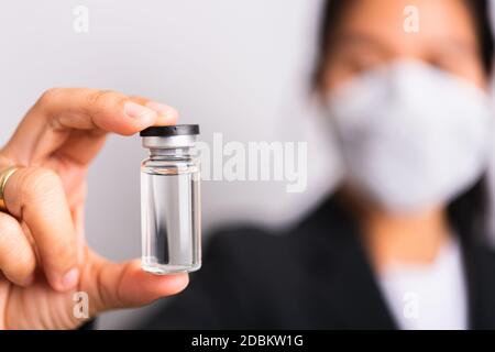 Asian woman doctor wearing surgical protective cloth face mask against coronavirus her hold ampoule bottle vaccine focus on  glass transparent, studio Stock Photo