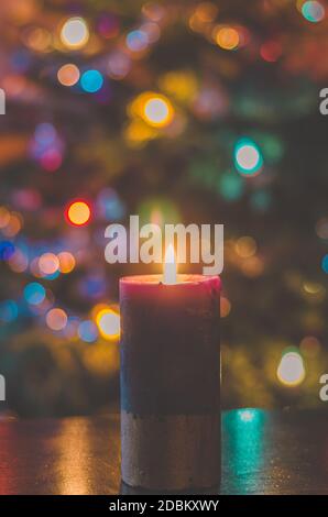 one burning candle concept with shining bokeh glittering ligts on christmas tree on dark background Stock Photo