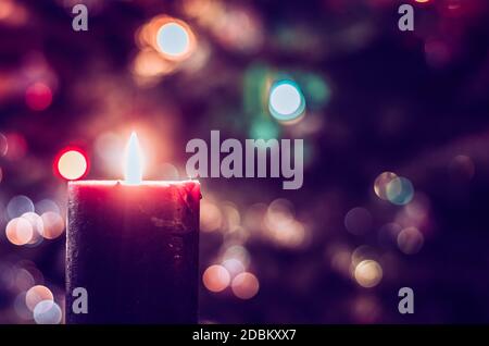 one burning candle concept with shining bokeh glittering ligts on christmas tree on dark background Stock Photo