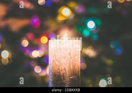 one burning candle concept with shining bokeh glittering ligts on christmas tree on dark background Stock Photo
