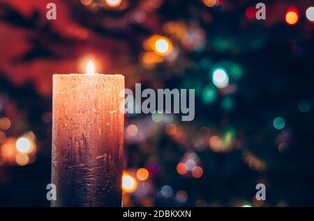 one burning candle concept with shining bokeh glittering ligts on christmas tree on dark background Stock Photo