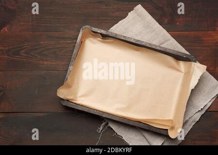 empty rectangular metal pan covered with brown parchment paper on a wooden table, top view Stock Photo