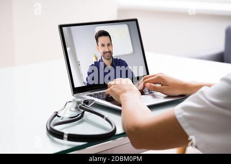 Doctor Talking To Male Patient Through Video Chat On Laptop At Desk Stock Photo