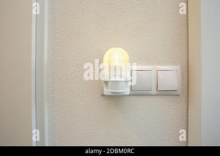 Night light plug in white socket on white wall turns on automatically in modern house Led light Stock Photo