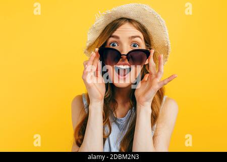 Shocked surprised girl in sunglasses and a summer hat, on a yellow background. Travel, vacation, summer Stock Photo
