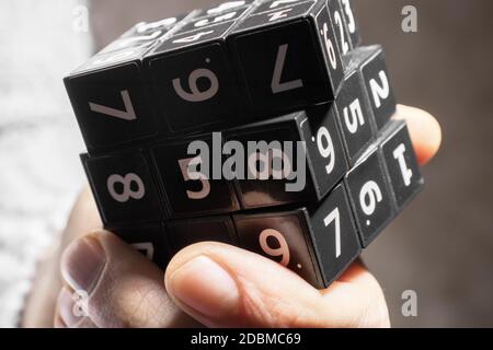 A man holds in his hands a black cube with numbers on its area for playing the Japanese game of Sudoku on a white background Stock Photo