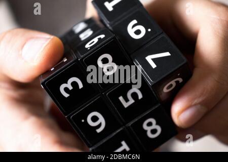 A man holds in his hands a black cube with numbers on its area for playing the Japanese game of Sudoku on a white background Stock Photo