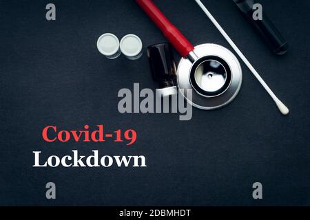 COVID-19 or CORONAVIRUS LOCKDOWN text with stethoscope, medical swab and vial on black background. Covid-19 or Coronavirus concept. Stock Photo