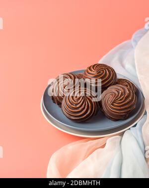 Traditional Russian vanilla marshmallows in chocolate glaze in blue and white plates on a pink background. Colorful table and silk textiles. Vertical Stock Photo