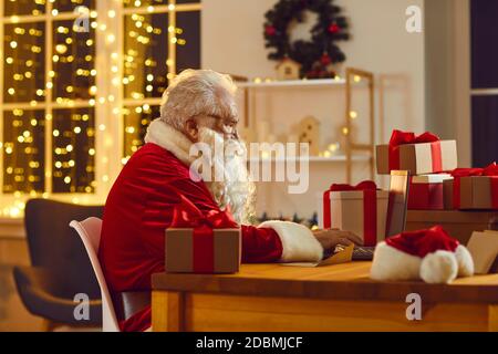 Santa Claus working on his laptop, answering emails and ordering presents delivery online Stock Photo