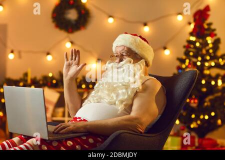 Grandpa wearing Santa's beard sitting in an armchair and video calling his family on Christmas Eve Stock Photo