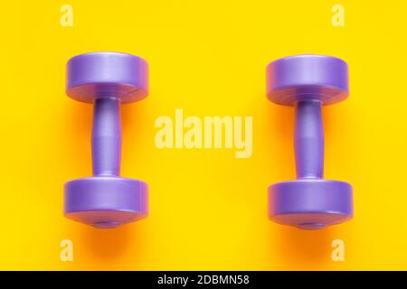 Two purple dumbbells lie separately on a yellow background Stock Photo