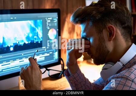 Fatigued young man taking off glasses rubbing tired eyes after computer work. Stock Photo