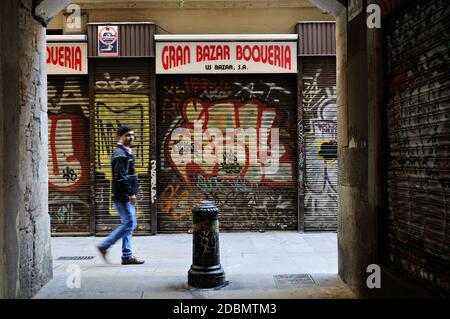 Man in front of the Gran Bazaar Boqueria closed by security blinds covered in graffiti, Barcelona, Catalonia, Spain Stock Photo