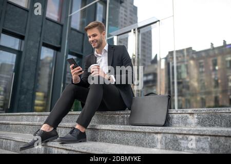 Elegant male businessman sitting on the steps and reading something online Stock Photo