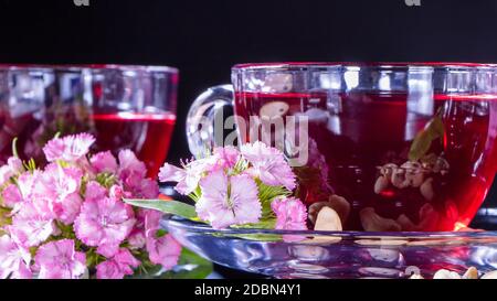 Hibiscus Red tea mug with carnation flowers close-up horizontal photo.English tea tradition.Medicinal therapy based on medicinal herbs and decoctions. Stock Photo