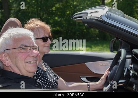 Happy older couple drives with a luxury convertible car Stock Photo