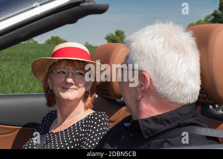 Happy older couple drives with a luxury convertible car Stock Photo