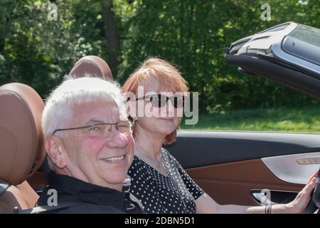 Happy older couple drives with a luxury convertible car on a sunny day Stock Photo