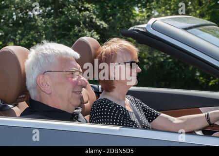 Happy older couple drives with a luxury convertible car Stock Photo