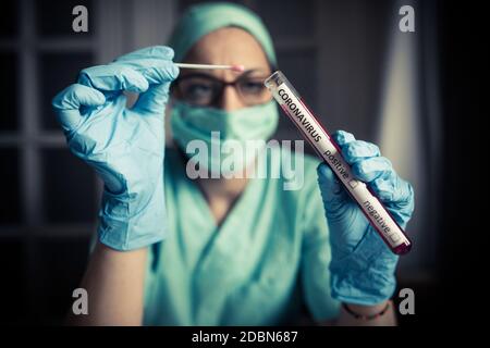 Conceptual photograph of a doctor holding and looking at a test tube while testing samples for presence of coronavirus (COVID-19). Stock Photo