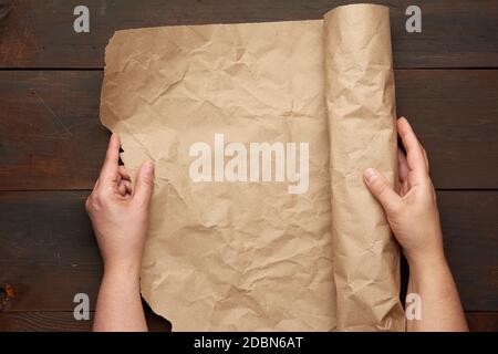 two female hands hold a rolled roll of brown craft paper on a wooden table, top view Stock Photo