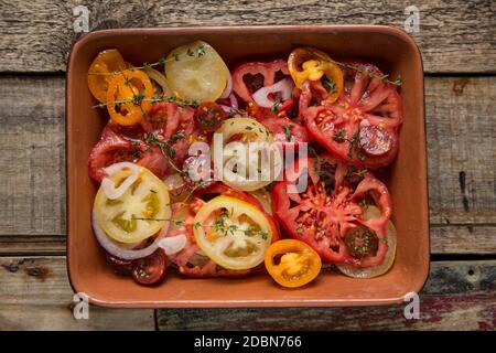 A selection of sliced heirloom tomatoes that have been served with a white wine vinegar and olive oil dressing, sliced red onion and fresh thyme. Wood Stock Photo