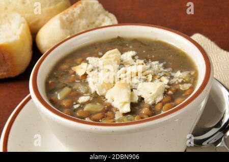 A cup of lentil soup with saltine crackers and dinner rolls in the background Stock Photo