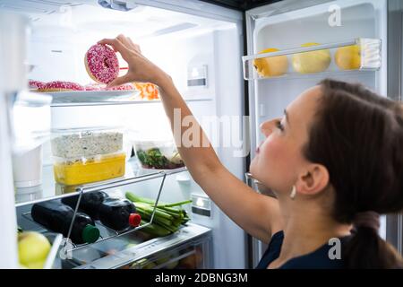 Woman On Diet Indulging In Kitchen Near Refrigerator Stock Photo