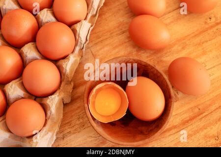 Cracked egg in bowl and egg shells on wooden table. Stock Photo