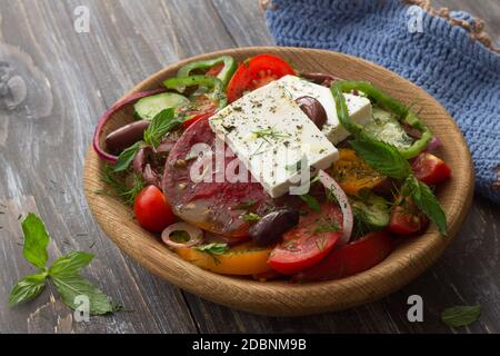 Homemade Greek salad from tomatoes, cucumbers, sweet peppers, cheese, olives and greens in a wooden bowl on a wooden table. Healthy delicious food Stock Photo