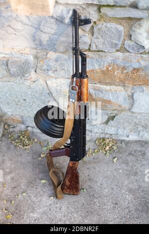 Kalashnikov AKM with high-capacity 75 rounds drum magazine near a stone wall