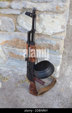 Kalashnikov AKM with high-capacity 75 rounds drum magazine near a stone wall
