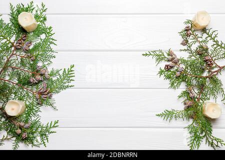 Conifer tree branches with cones and candles on white wooden background. New Year postcard template, copy space Stock Photo
