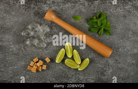 Close up mojito cocktail ingredients set flat lay, wooden muddler, brown sugar, heap of fresh green mint leaves, lime slices and ice cubes on table, e Stock Photo