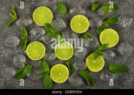 Close up flat lay of lime slices, fresh green mint leaves and ice cubes on grunge gray stone table surface, elevated top view, directly above Stock Photo