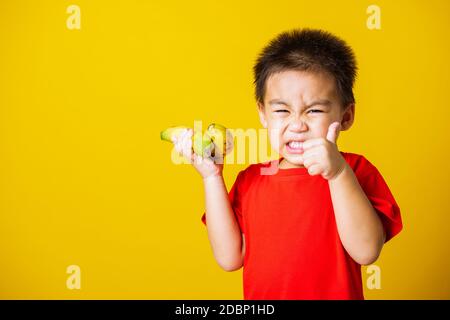 Happy portrait Asian child or kid cute little boy attractive smile wearing red t-shirt playing holds bananas and show finger thumb for good sign, stud Stock Photo