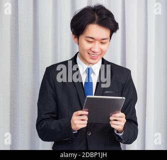 Work from home, Asian young businessman wear suit video conference call or facetime he smiling using smart digital tablet computer touching on screen Stock Photo
