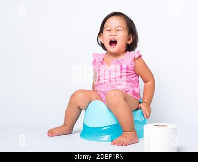 Asian little cute baby child girl education training to sitting on blue chamber pot or potty with toilet paper rolls, studio shot isolated on white ba Stock Photo