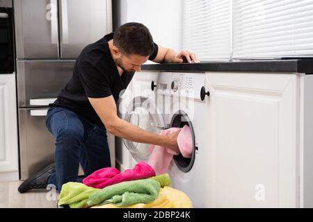 Man Loading Clothes Into Washing Machine In Kitchen Stock Photo