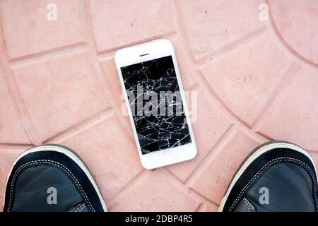 broken smartphone screen. Feet and smartphone with a broken phone screen on the tile floor. Top view broken phone Stock Photo