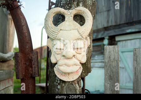 Old african ancient handmade mask on wooden fence near house. African culture traditional masks close up Stock Photo