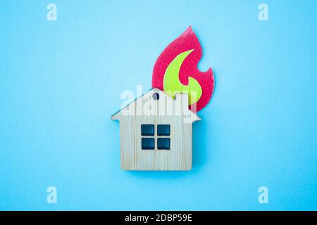 Fire house, insurance and mortgage concept. Small wooden house toy and paper fire shape on blue background top view Stock Photo