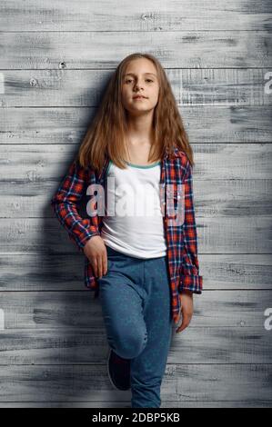 Adorable little girl standing at the wall in studio. Kid isolated on wooden background, child emotion, schoolgirl photo session Stock Photo