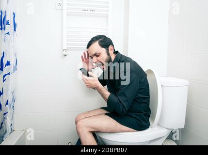 man sitting in toilet and talking on phone Stock Photo