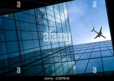 Airplane flying above modern glass office building. Perspective view of futuristic business building. Exterior of skyscraper building. Business trip. Stock Photo