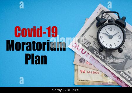COVID19 MORATORIUM PLAN text with alarm clock and banknotes currencies on blue background. Coronavirus Covid19 and Business Concept Stock Photo