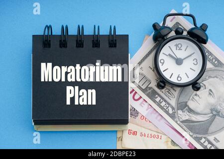 MORATORIUM PLAN text with alarm clock, banknotes currencies on blue background. Coronavirus Covid19 and Business Concept Stock Photo